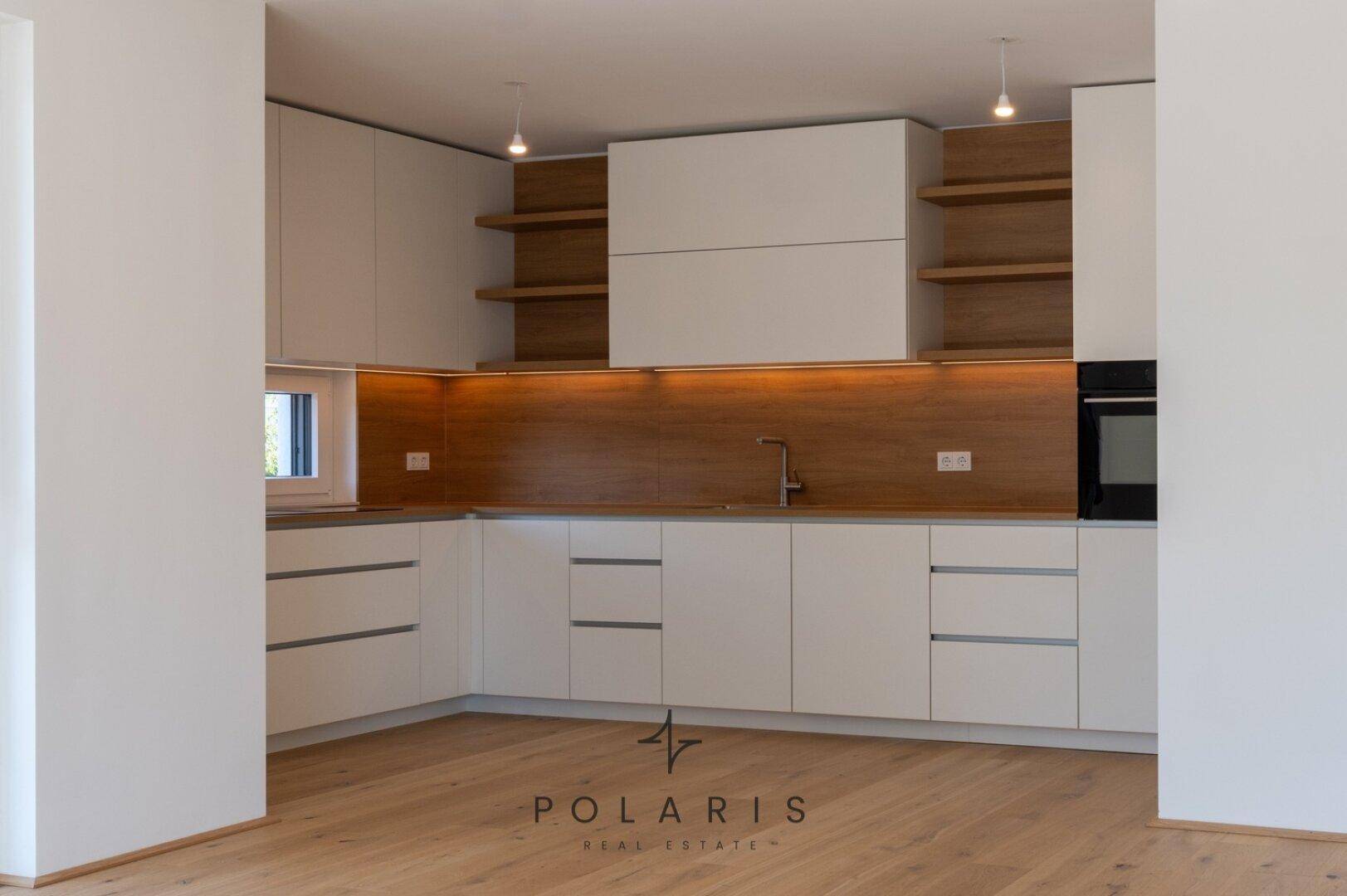 Geräumige, offene Küche mit weißen Schränken, Holzrückwand und integrierten Geräten, ideal für modernes Wohnen.
