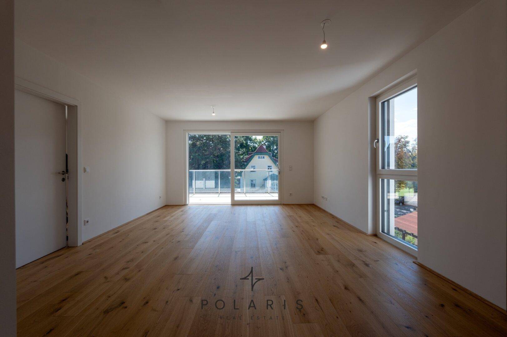 Geräumiges Wohnzimmer mit Holzboden und Zugang zu einem Balkon, der viel Licht bietet.