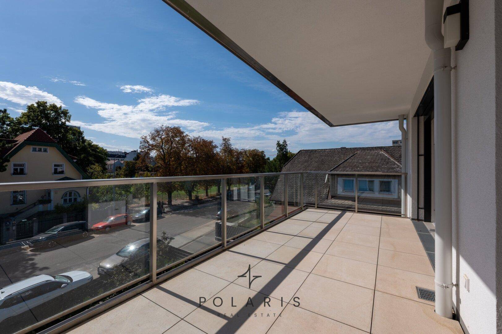Großer Balkon mit Fliesenboden und Glasgeländer, bietet einen sonnigen Platz im Freien.