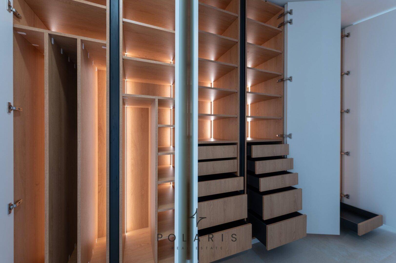 Offener Einbauschrank im Flur mit beleuchteten Fächern und Schubladen, bietet viel Stauraum.