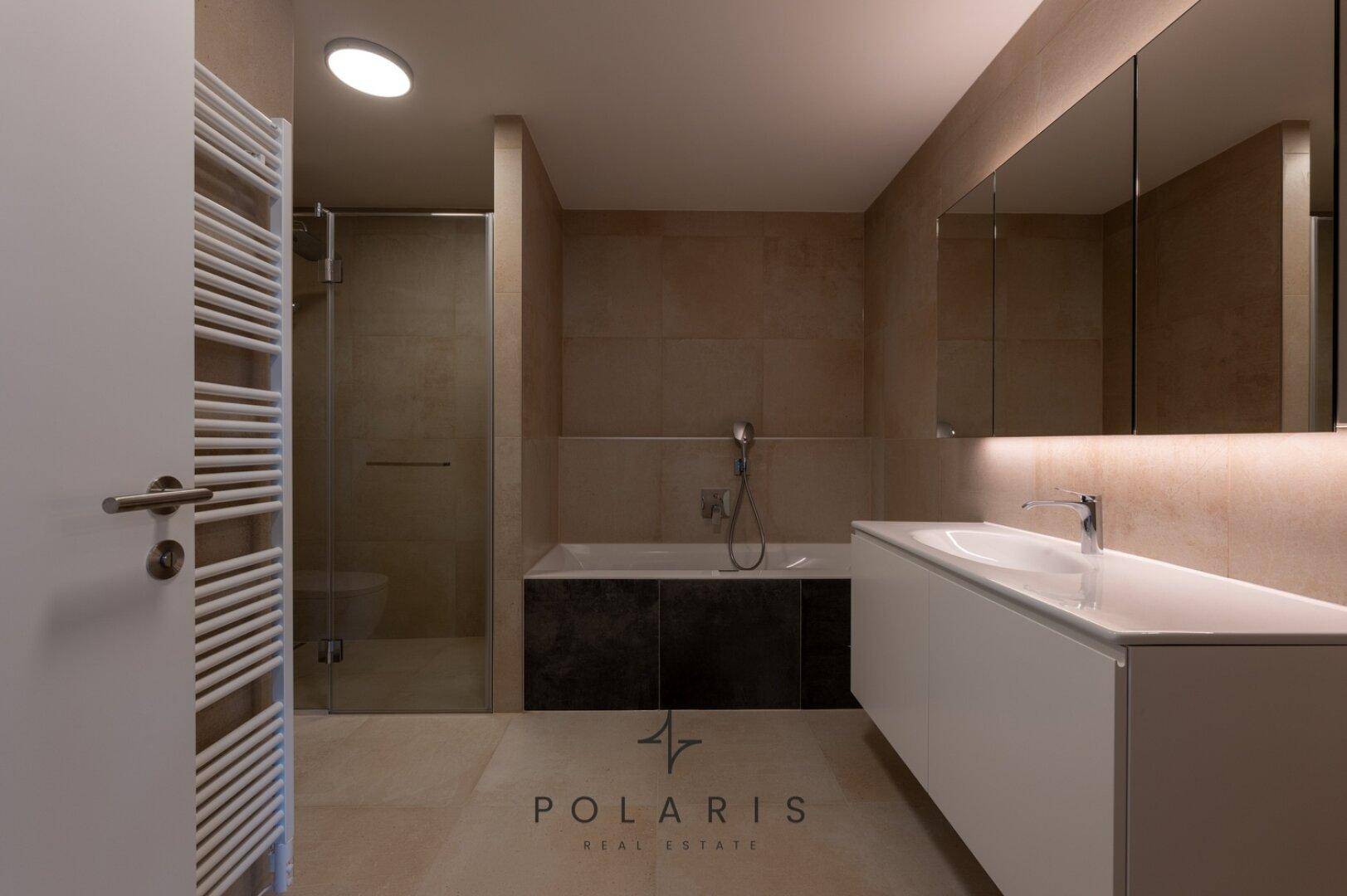 Modernes Badezimmer mit Badewanne, Dusche und großem Waschtisch, beleuchtet von indirektem Licht.