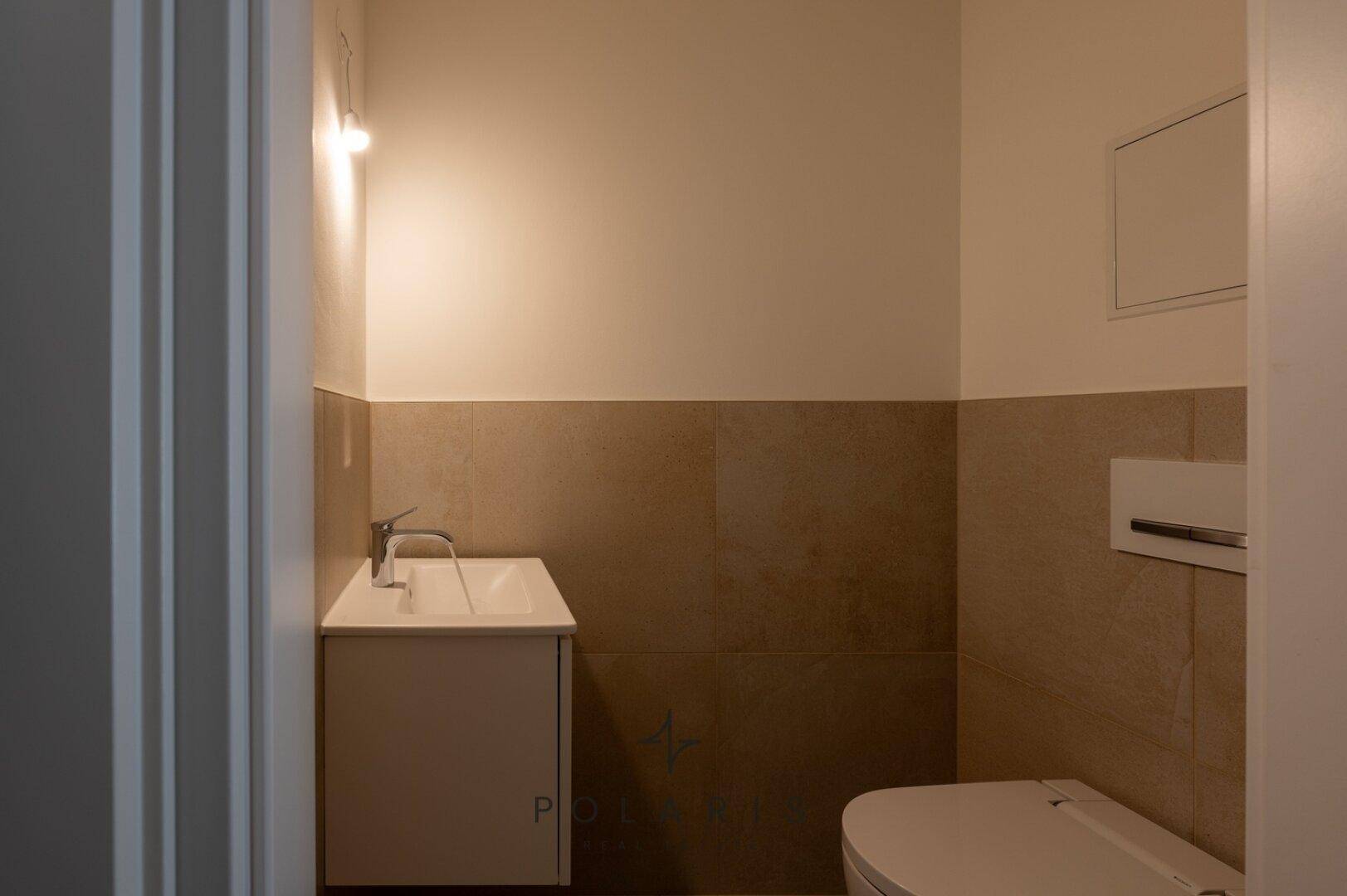 Modernes Gäste-WC mit kleinem Waschtisch und wandhängendem WC, in neutralen Farben gehalten.