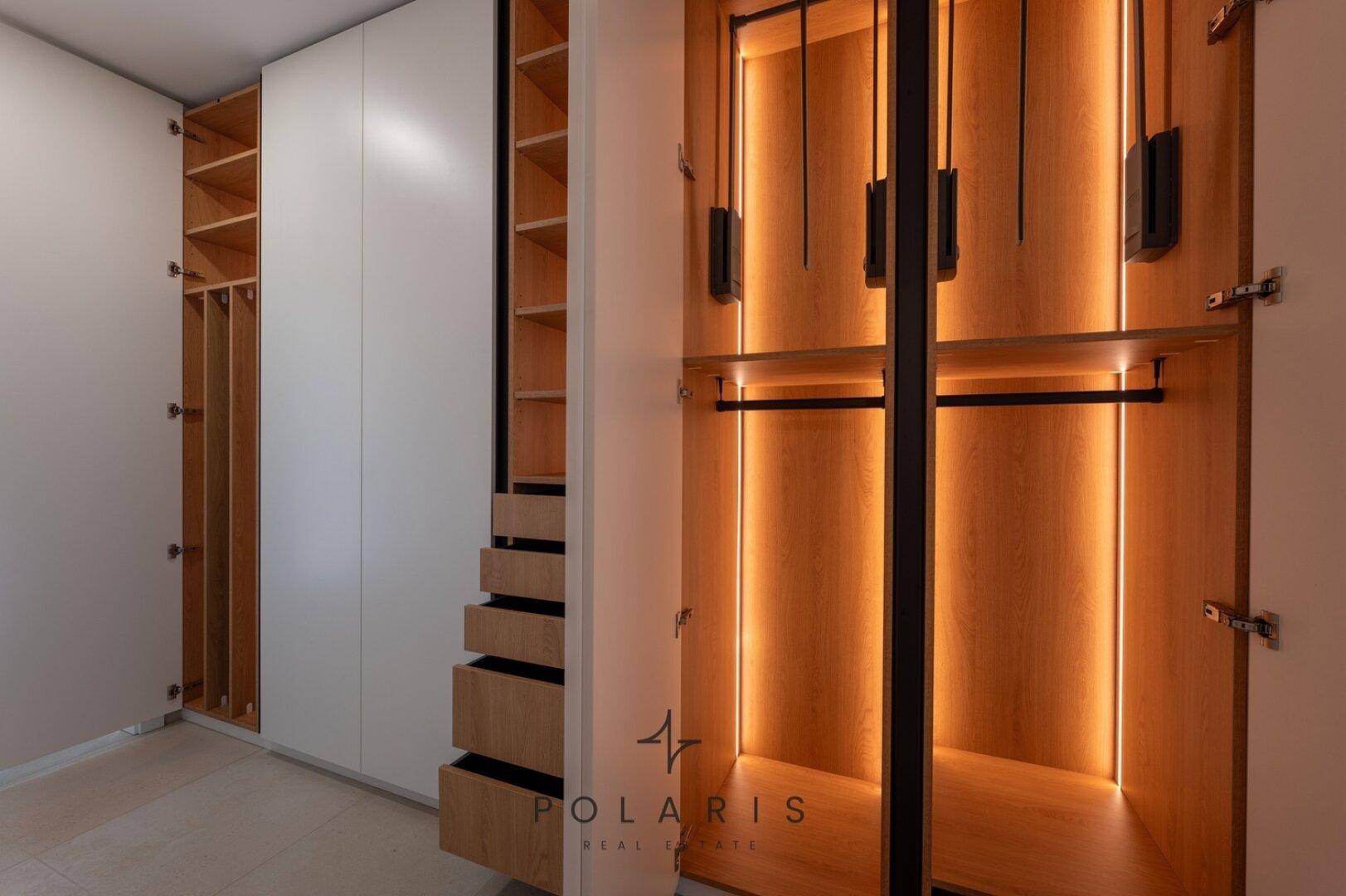 Beleuchteter Einbauschrank im Flur mit Kleiderstangen und Regalen, ideal für Organisation.