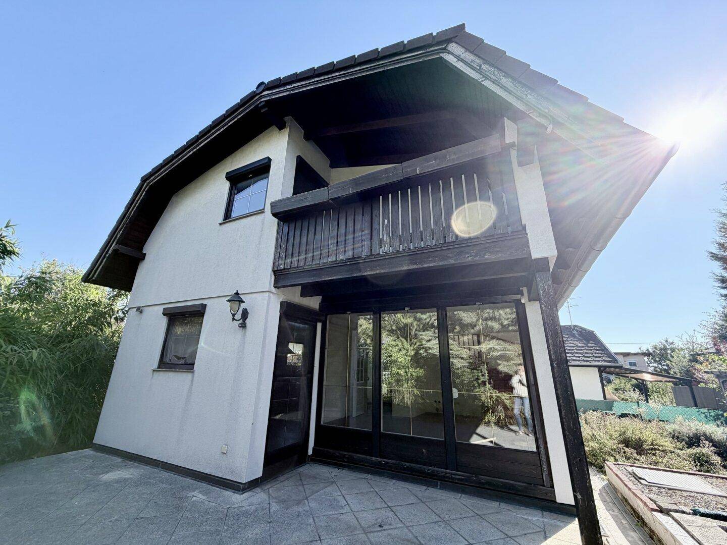Sonnige Außenansicht des Hauses mit Terrasse und Balkon, umgeben von viel Grün.