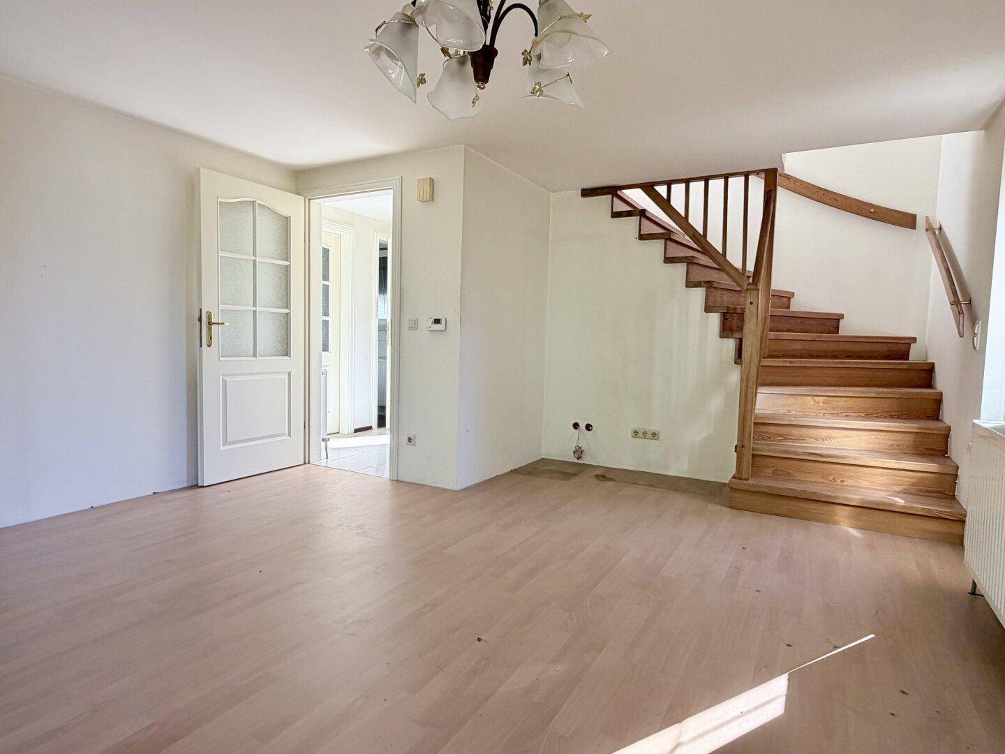 Heller Wohnbereich mit Holztreppe und Laminatboden, bereit für individuelle Gestaltung.