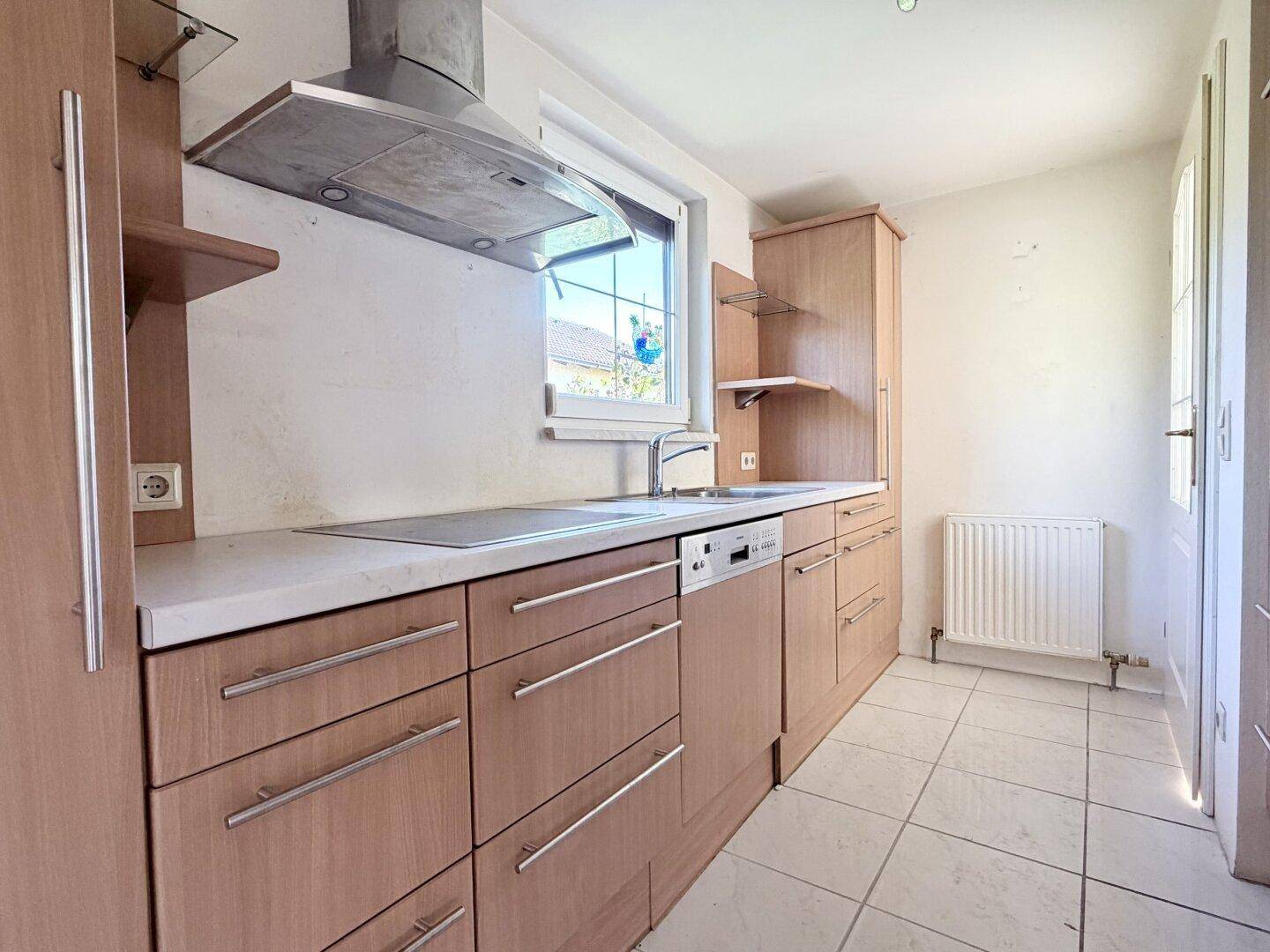 Funktionale Küche mit Holzschränken, Spülmaschine und Fenster, bereit zur Modernisierung.