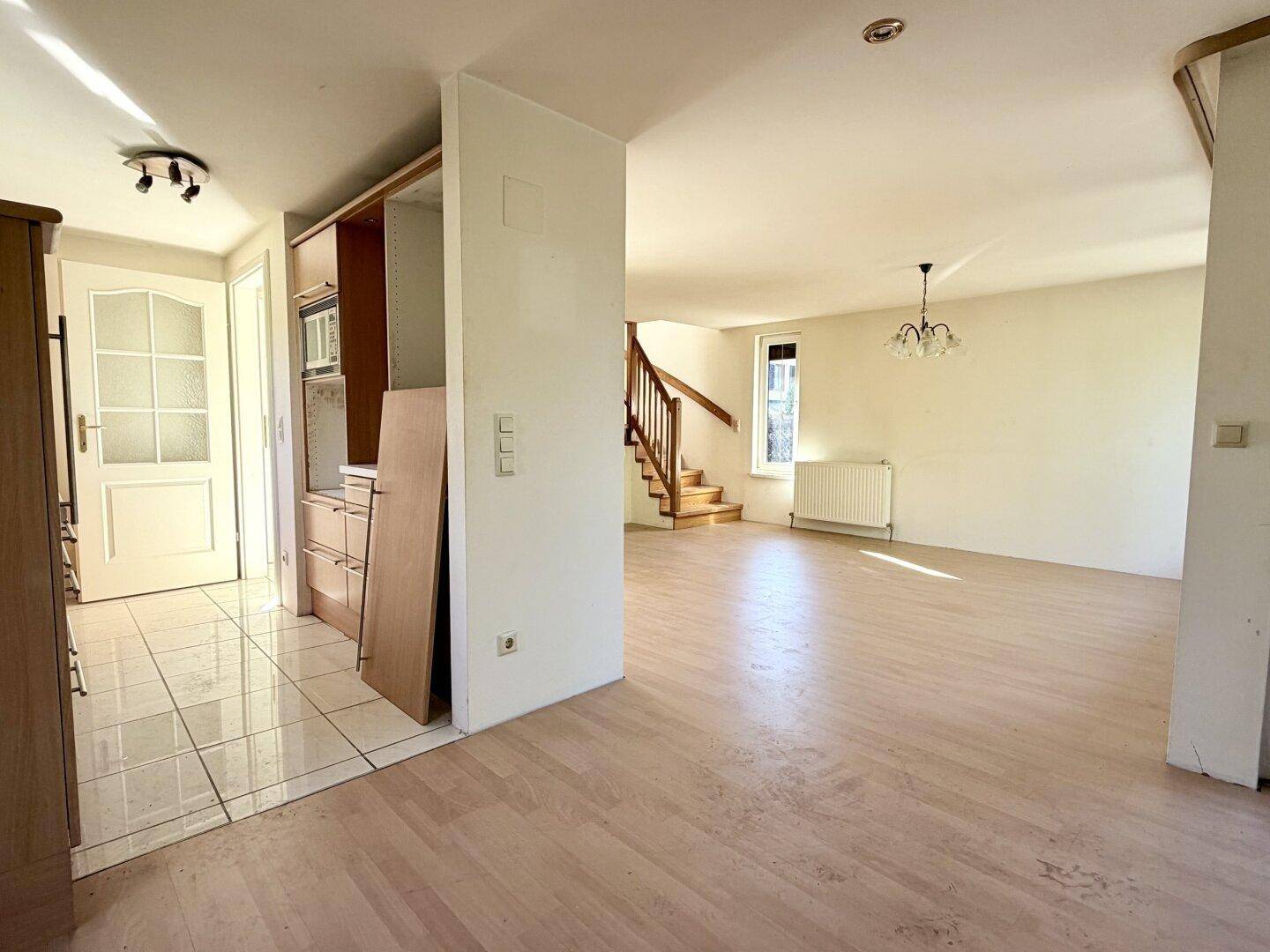 Offener Wohnbereich mit Übergang von Fliesen zu Laminatboden und Blick zur Holztreppe.