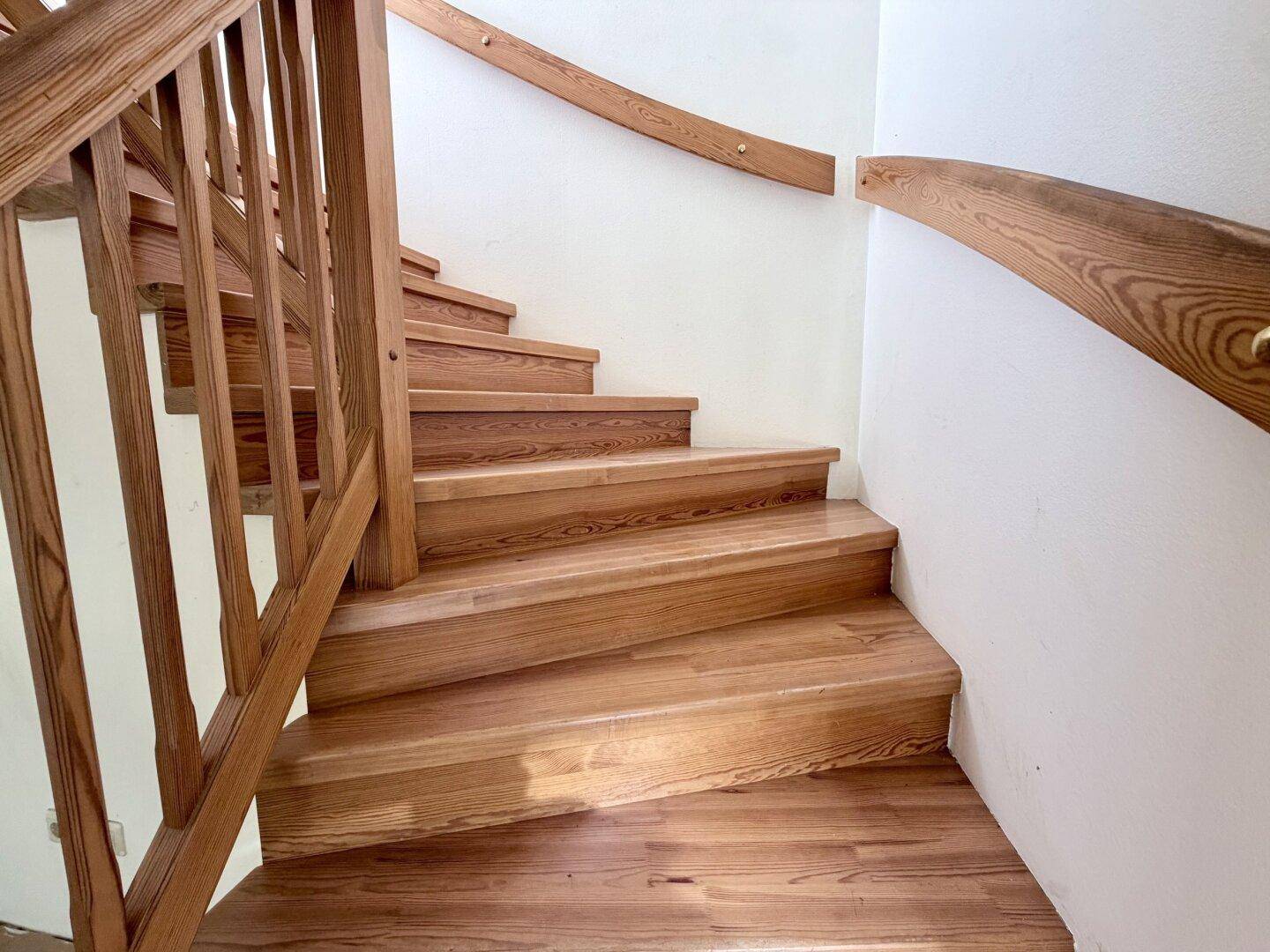 Geschwungene Holztreppe mit elegantem Geländer, die die verschiedenen Etagen verbindet.