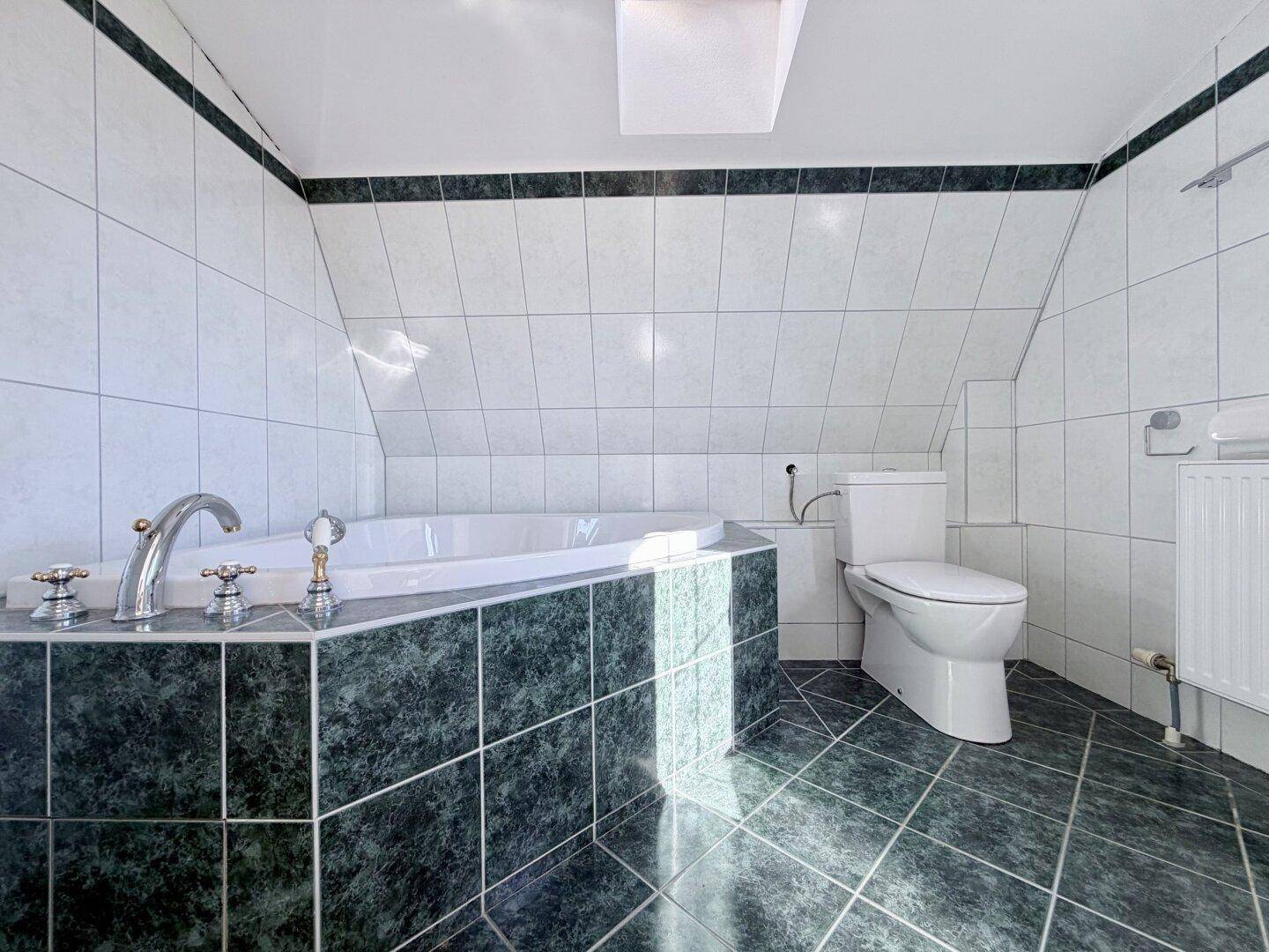 Gefliestes Badezimmer mit Eckbadewanne, WC und Dachschräge, bietet Entspannung.