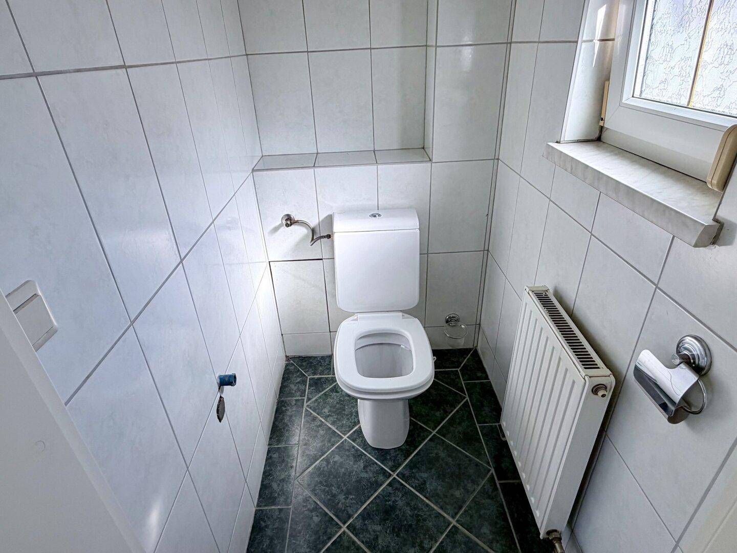 Kleines, hell gefliestes Gäste-WC mit Fenster und Heizkörper, funktional und sauber.