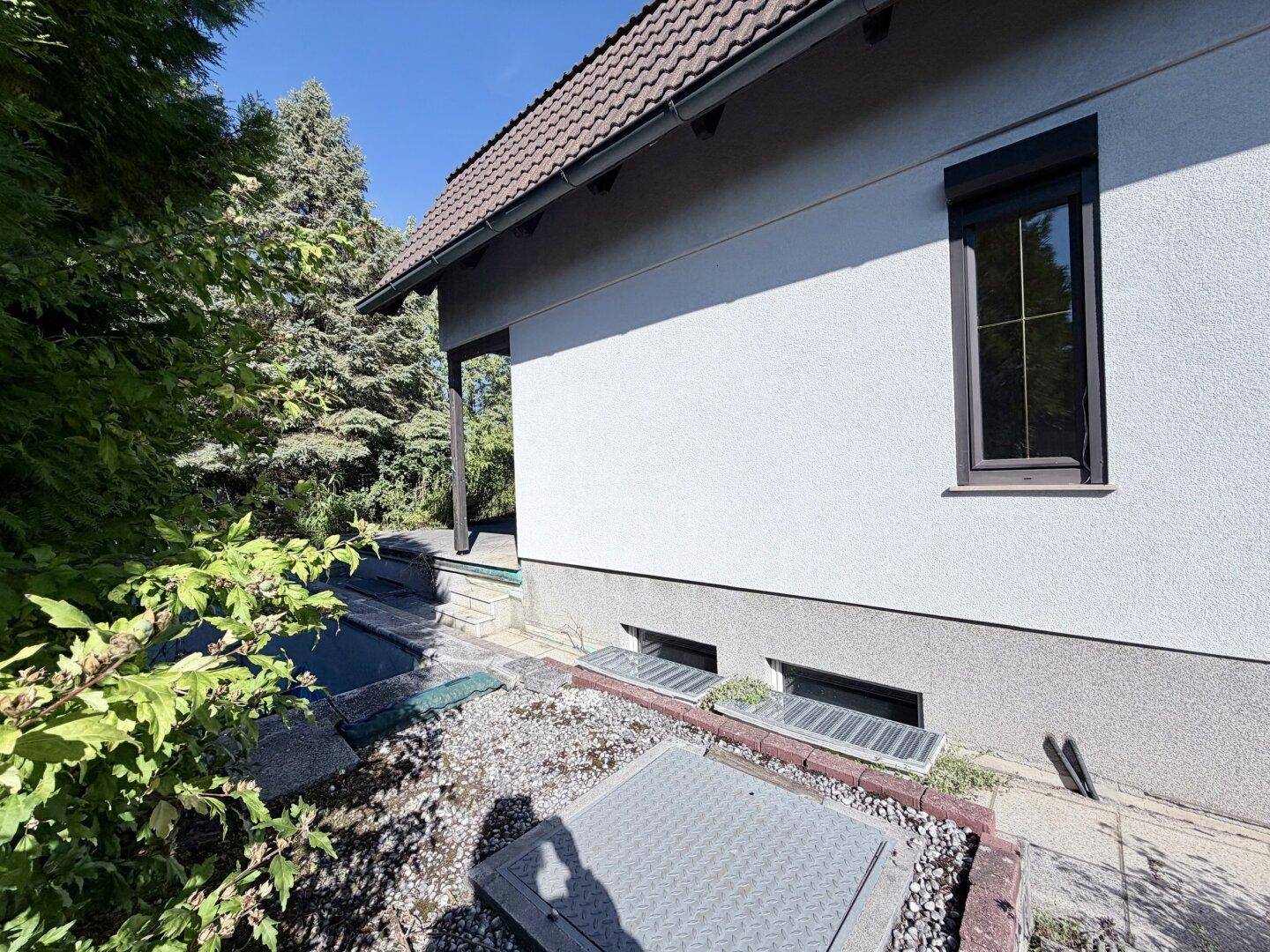 Seitenansicht des Hauses mit Kellerfenstern und Zugang zum Gartenbereich.