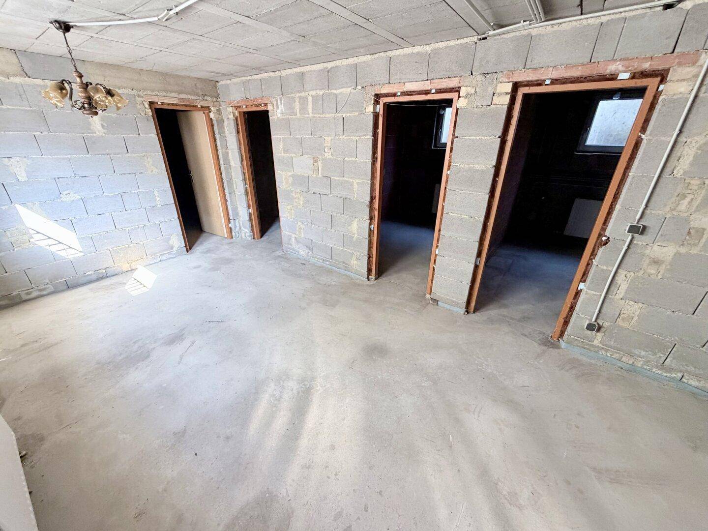 Großer Kellerraum mit mehreren Türöffnungen und Betonboden, ideal für Ausbauprojekte.