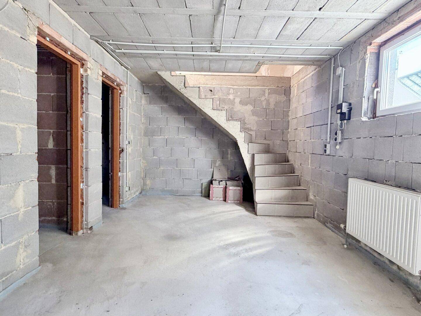 Unausgebauter Kellerraum mit Betonwänden und Treppenzugang, bietet viel Stauraum.