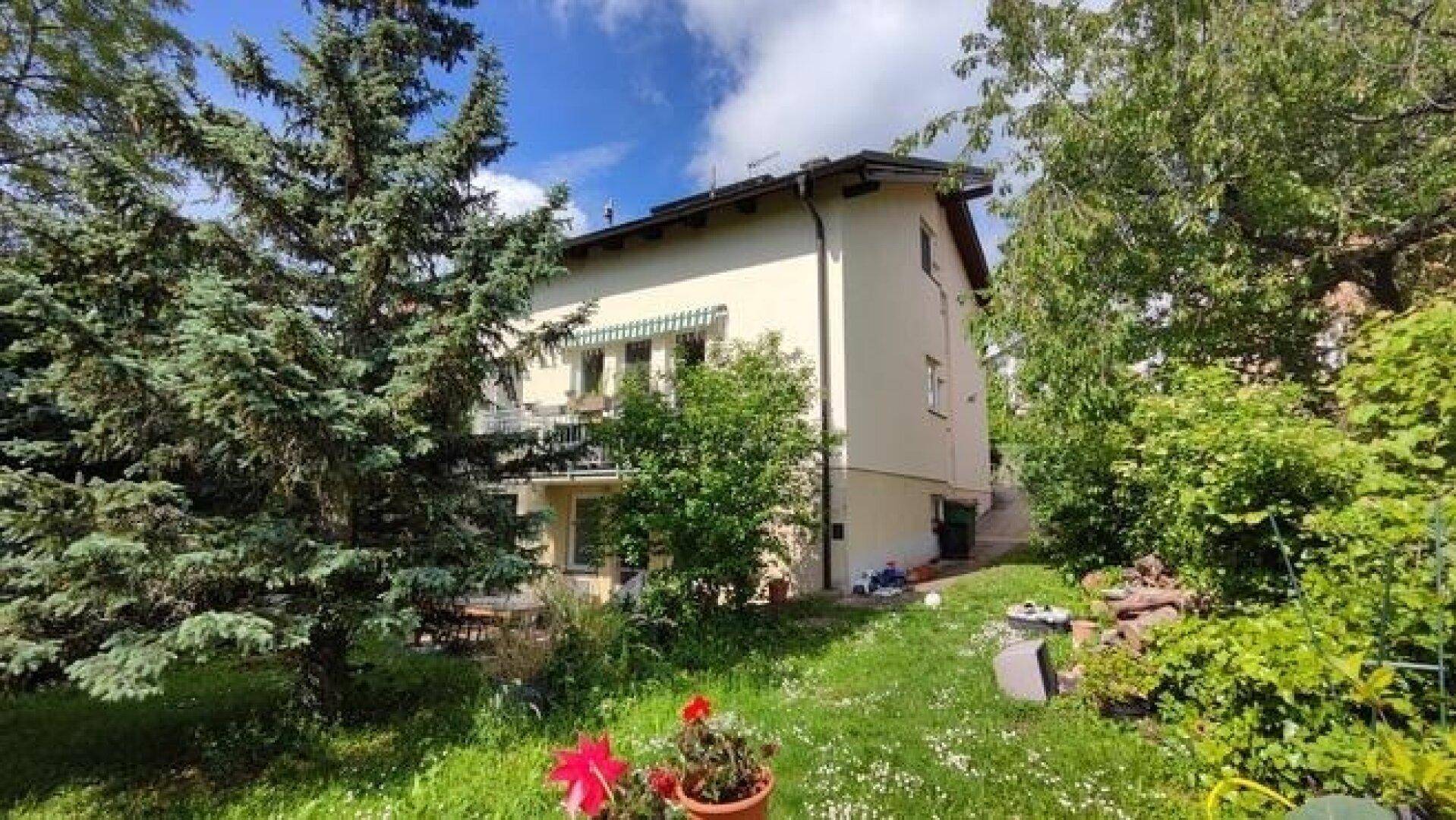 Weitläufiger Garten mit grüner Rasenfläche, Bäumen und einer Markise am Haus.