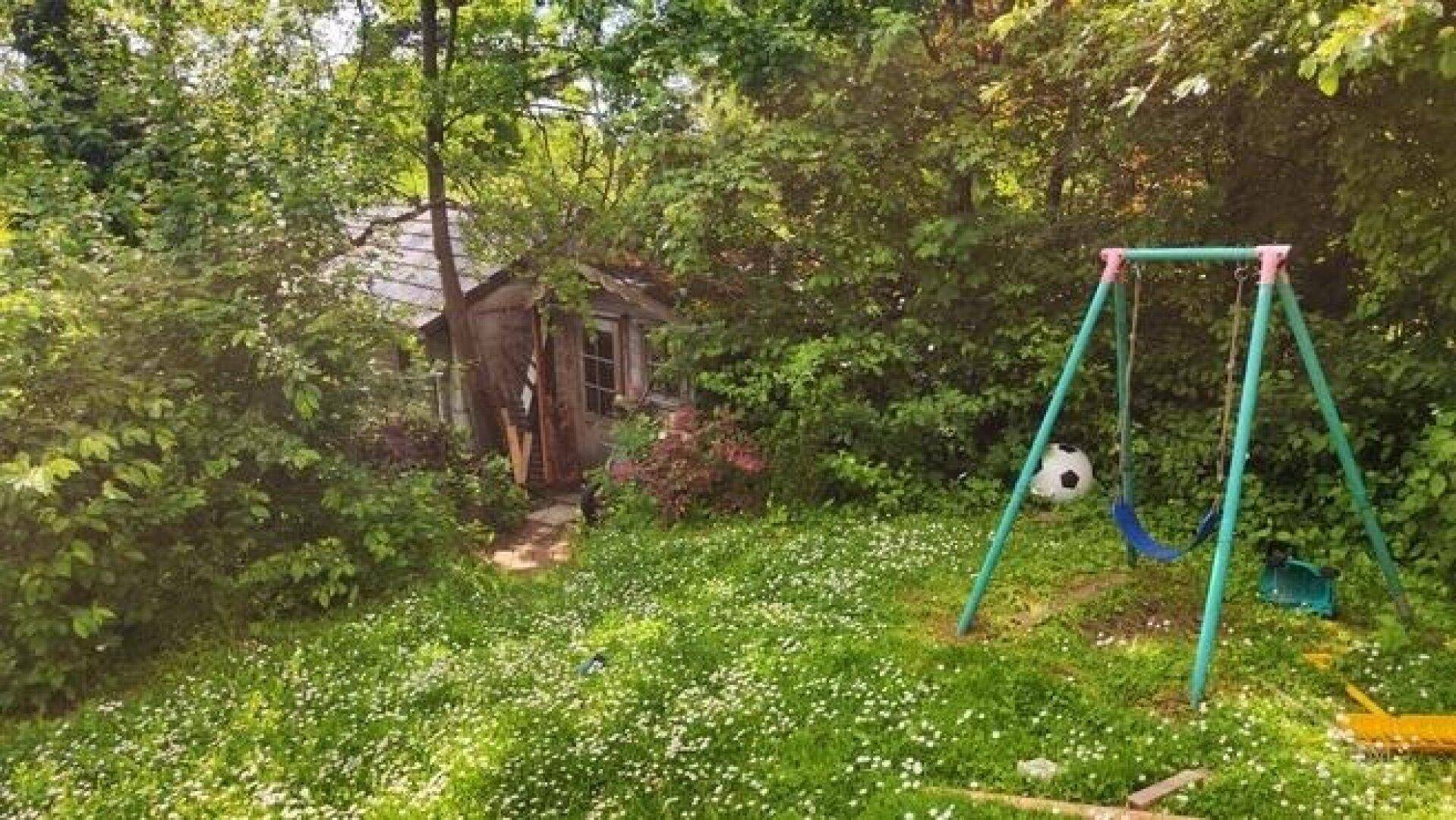 Teil des Gartens mit einem kleinen Holzschuppen und einem Kinderspielplatz mit Schaukel.