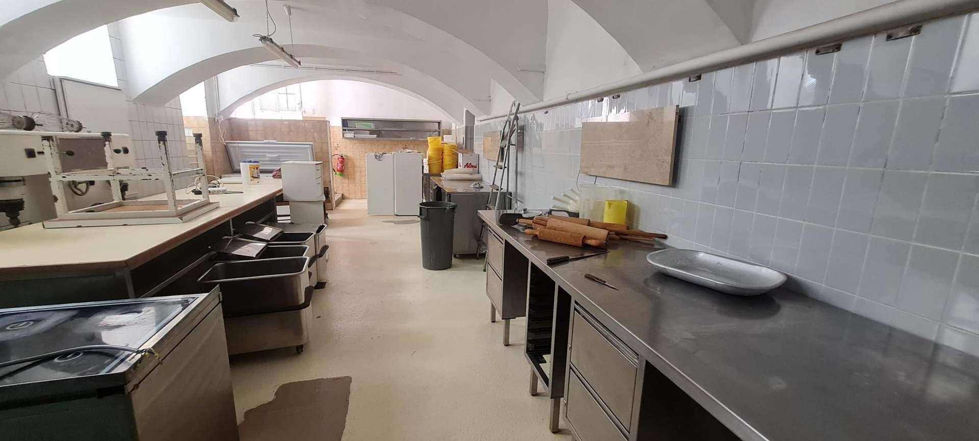 Langer Gang einer Gewerbeküche mit Edelstahl-Arbeitsflächen, professionellen Geräten und einem hellen Gewölbedach.