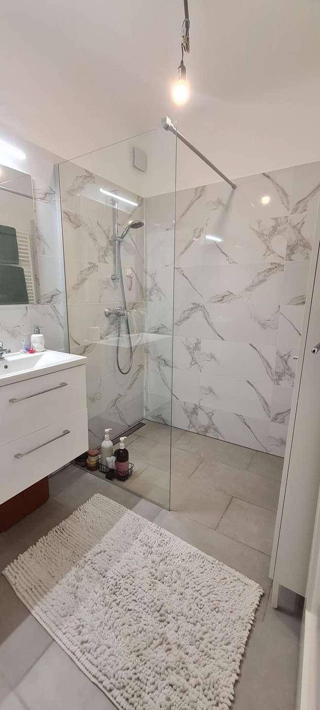 Elegantes Badezimmer mit einer geräumigen begehbaren Dusche und Fliesen in Marmoroptik.