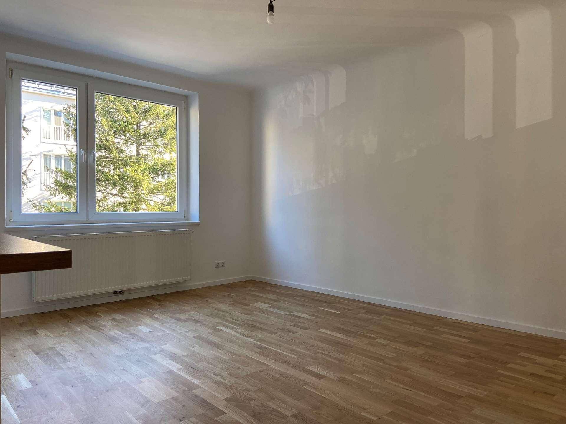 Lichtdurchflutetes Zimmer mit Parkettboden und einem Fenster, das einen Blick ins Grüne bietet.