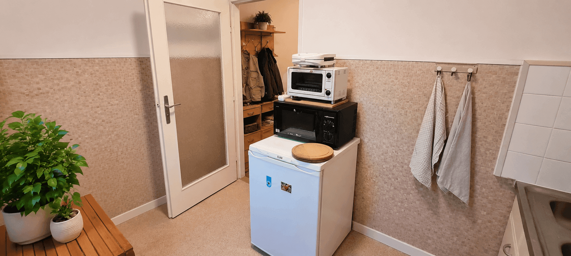 Küchenbereich mit Kühlschrank, Mikrowelle und Zugang zu einem weiteren Raum.