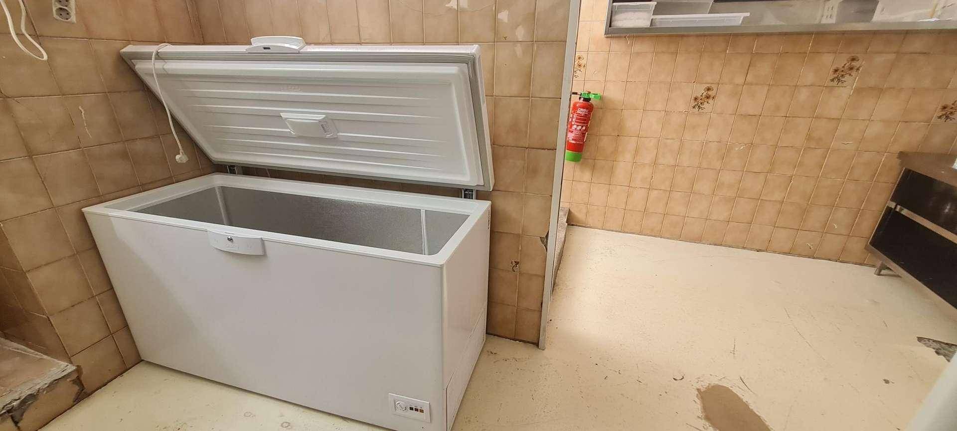 Ein großer, offener Gefrierschrank in einem Raum mit braunen Fliesen, bereit zur Befüllung oder Entnahme.