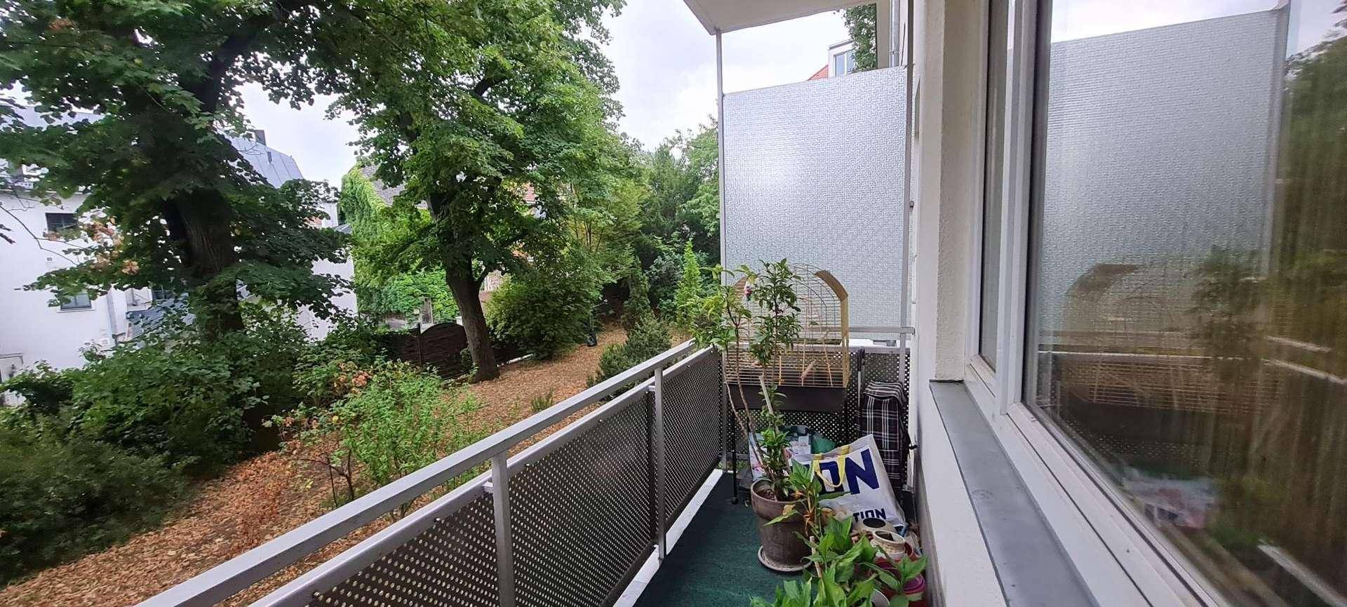 Balkon mit Metallgeländer und weitem Blick auf die grüne Umgebung und Bäume.