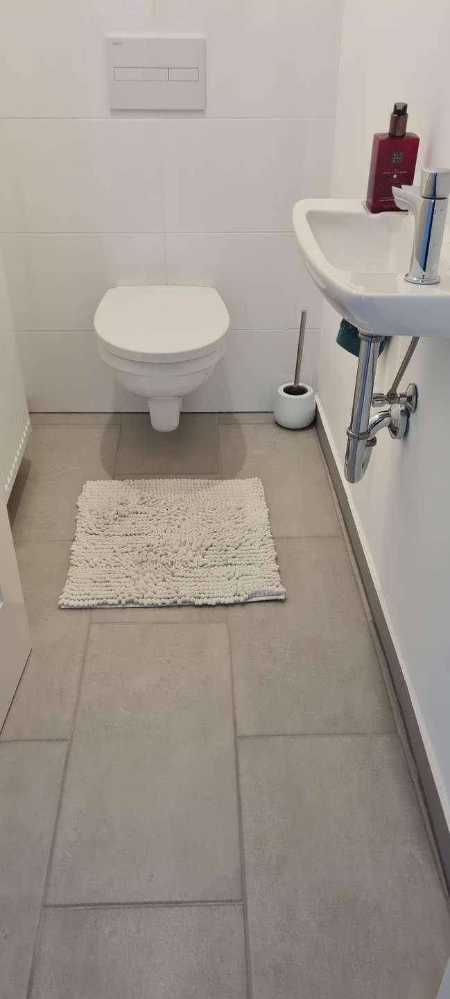 Modernes Gäste-WC mit wandhängendem WC, kleinem Waschbecken und grauen Fliesen.