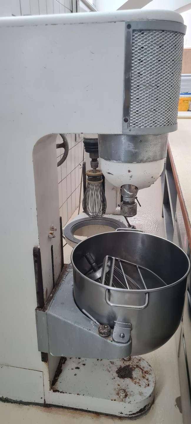 Nahaufnahme einer großen industriellen Küchenmaschine mit Rührschüssel und Schneebesen, ideal für Backwaren.