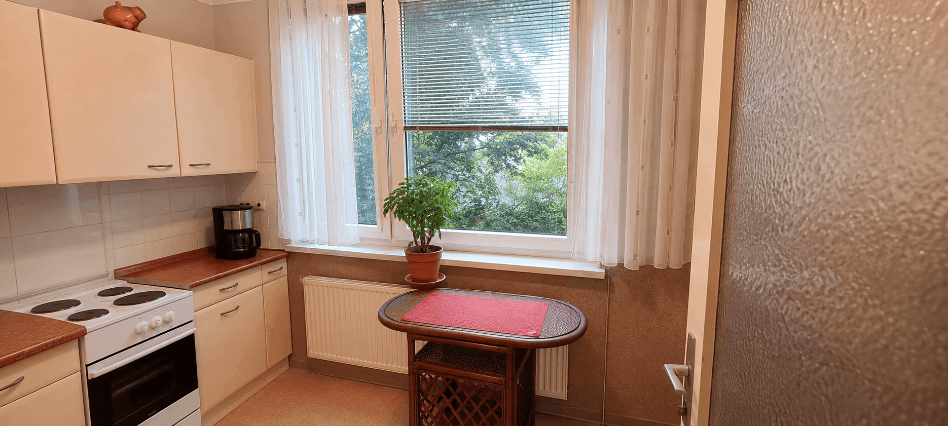 Helle Küche mit Essbereich am Fenster und Blick auf die Bäume.