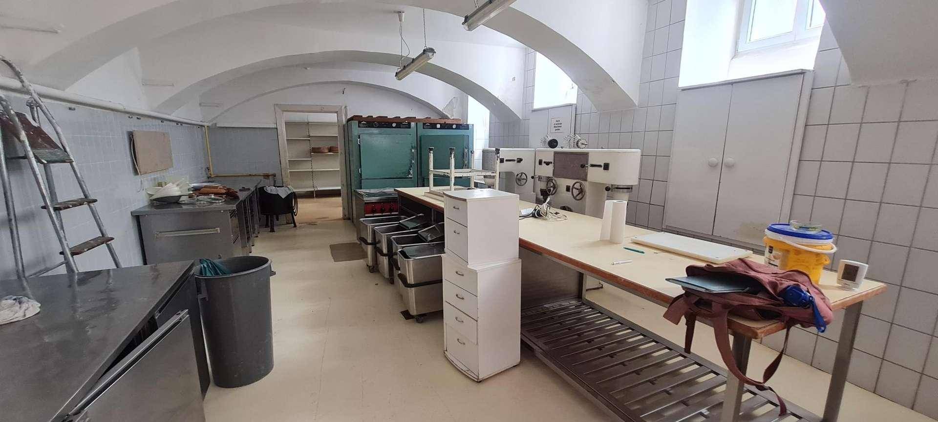 Geräumige Gewerbeküche mit verschiedenen professionellen Geräten, Edelstahl-Arbeitsflächen und einem hohen Gewölbedach.