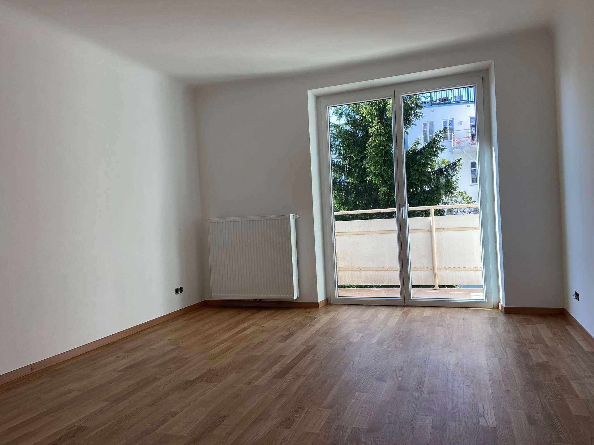 Geräumiges, helles Zimmer mit Parkettboden und direktem Zugang zu einem Balkon.