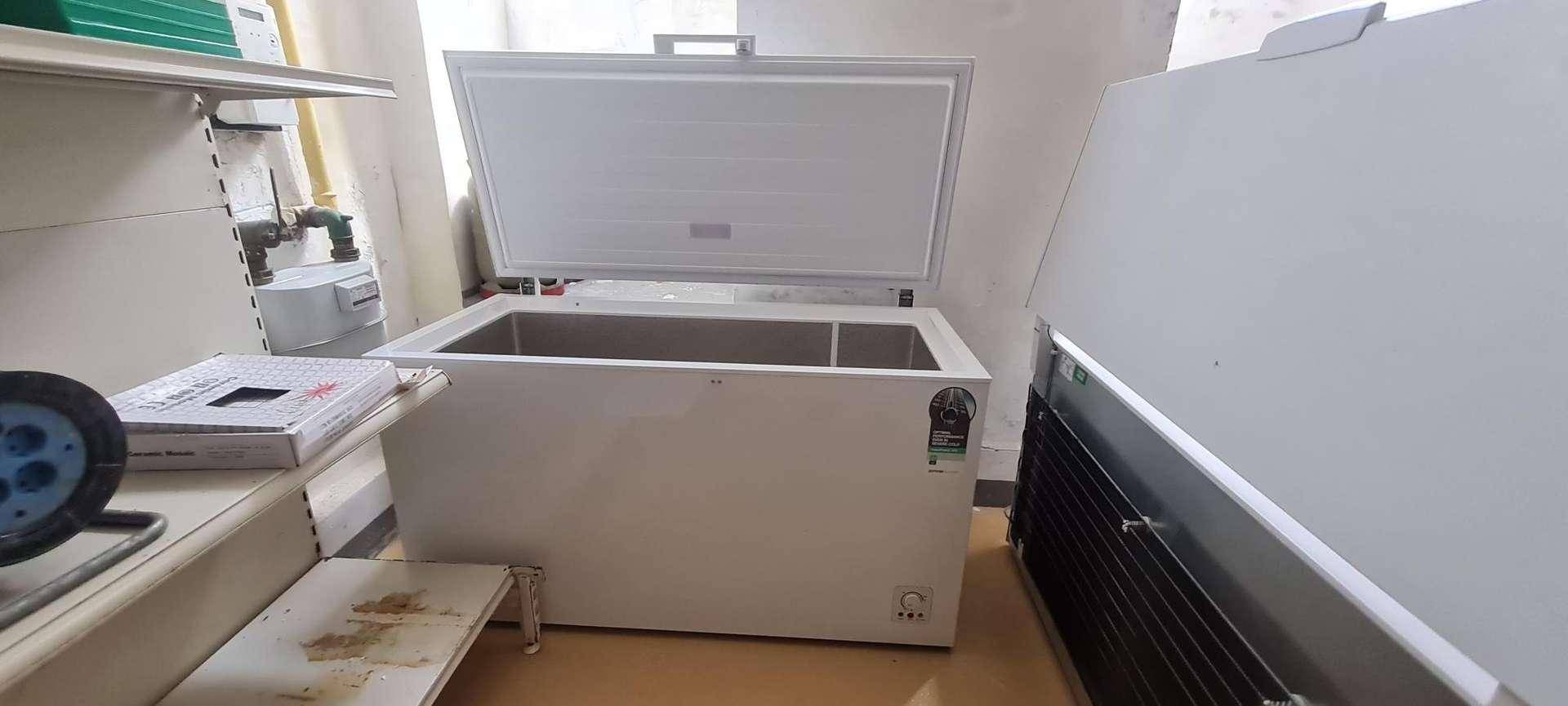 Ein offener weißer Gefrierschrank in einem Lagerraum, umgeben von Regalen und Versorgungsleitungen.