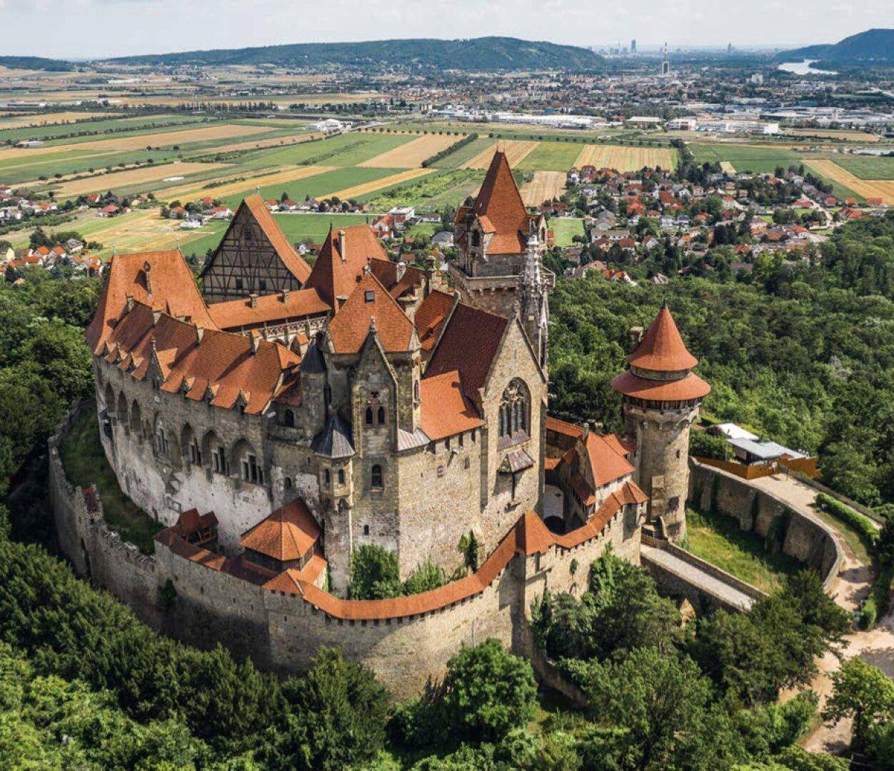 Beeindruckende Luftaufnahme der historischen Burg Kreuzenstein, umgeben von Wäldern und einer Stadt.