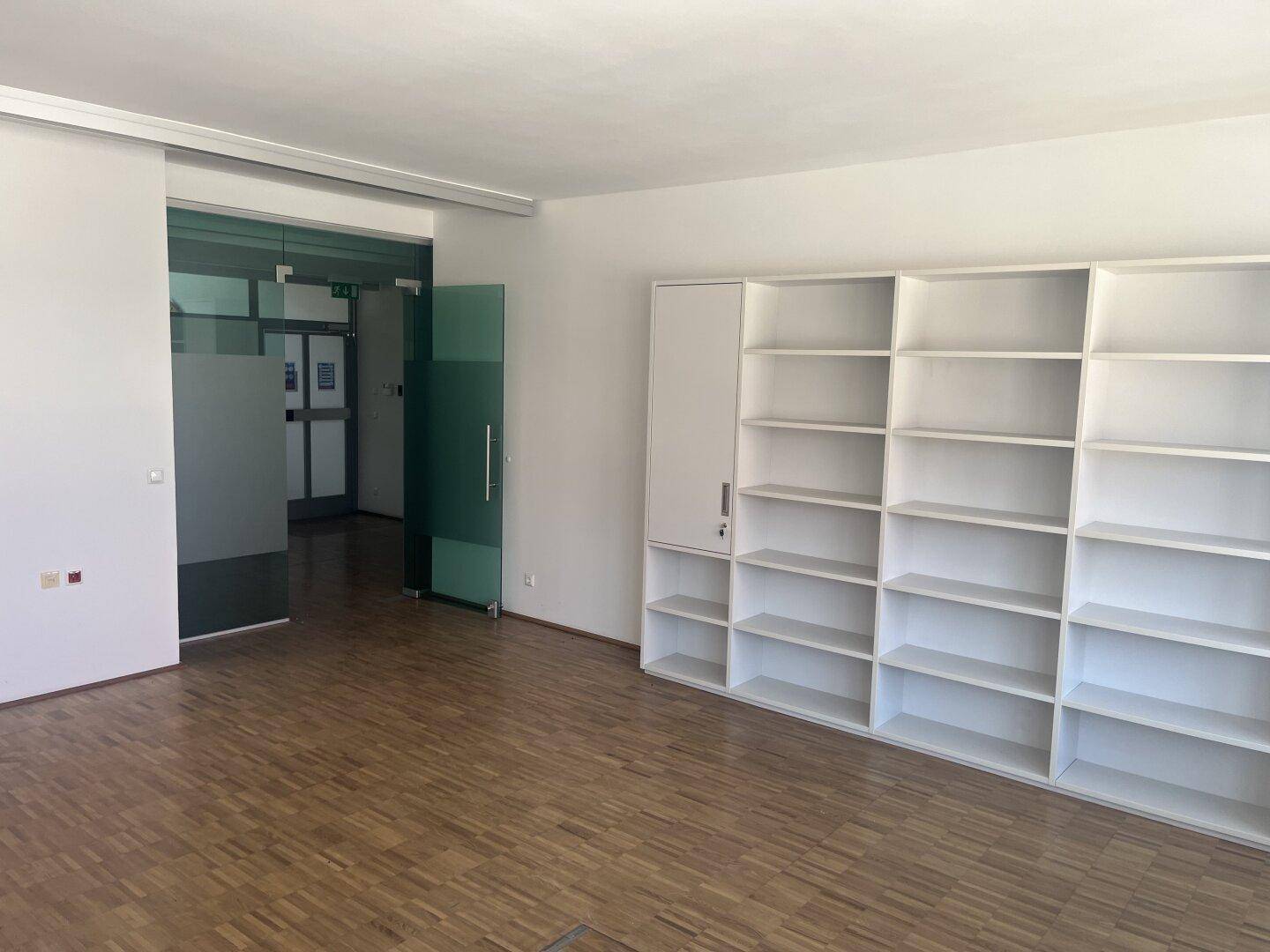 Geräumiges Büro mit Holzparkettboden und einem großen weißen Regal, das viel Stauraum bietet.