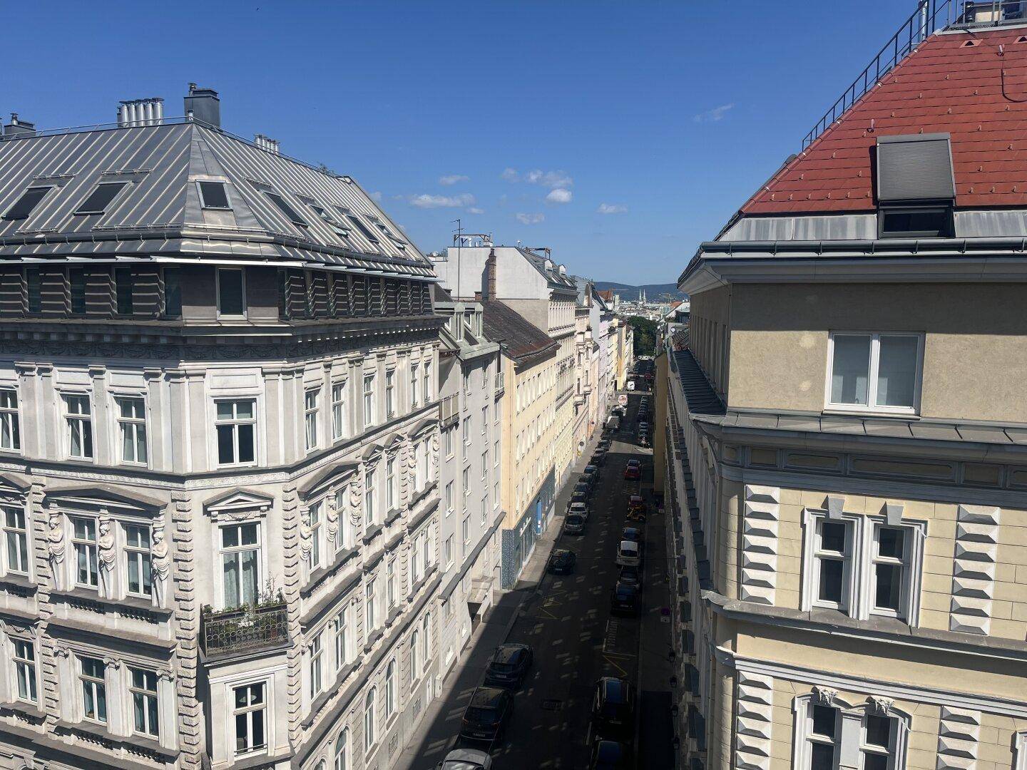 Panoramablick über eine belebte Stadtstraße mit historischen Gebäuden und einem klaren blauen Himmel.