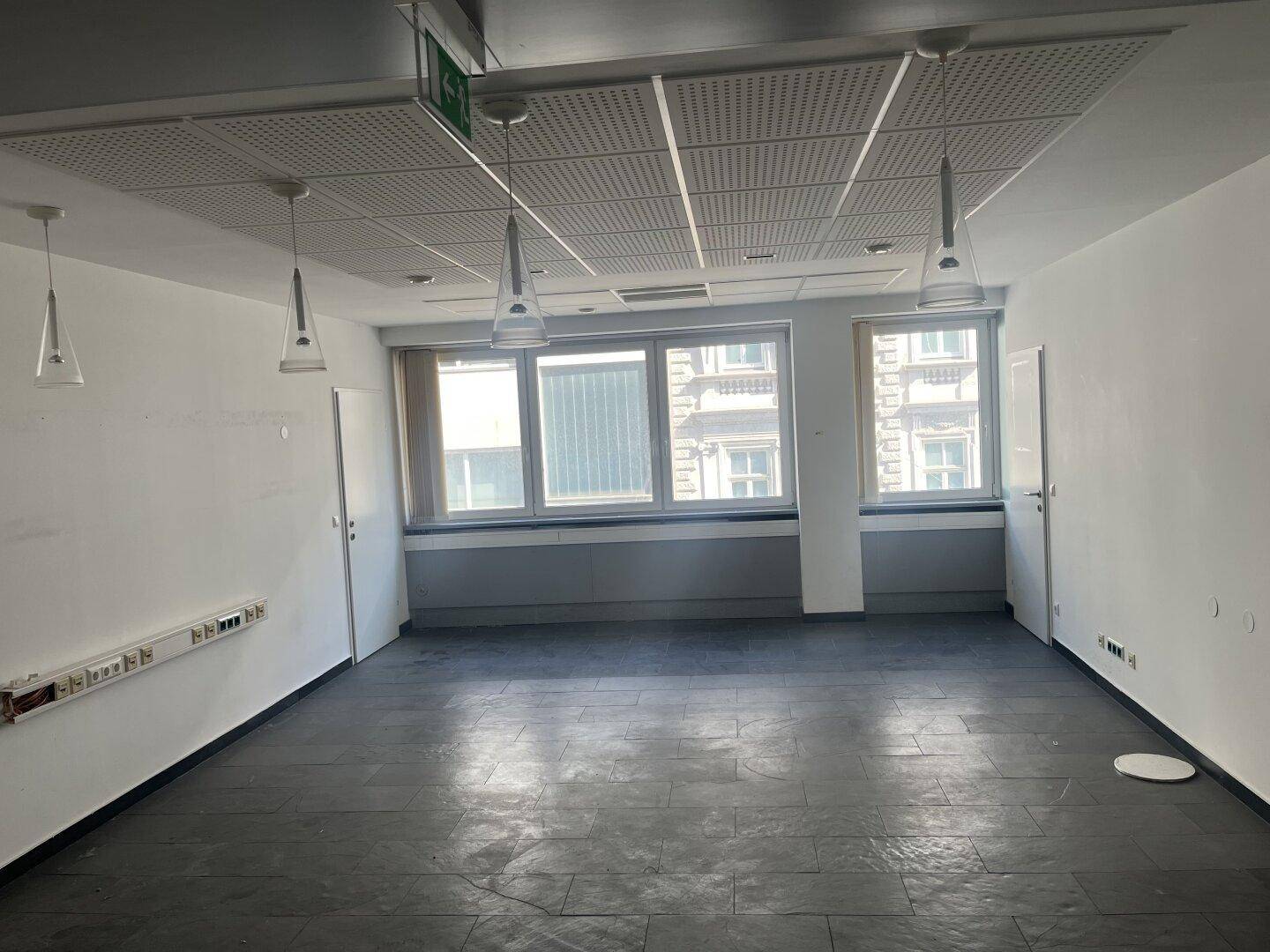 Büro mit dunklem Fliesenboden, großen Fenstern und modernen Hängelampen an der Decke.