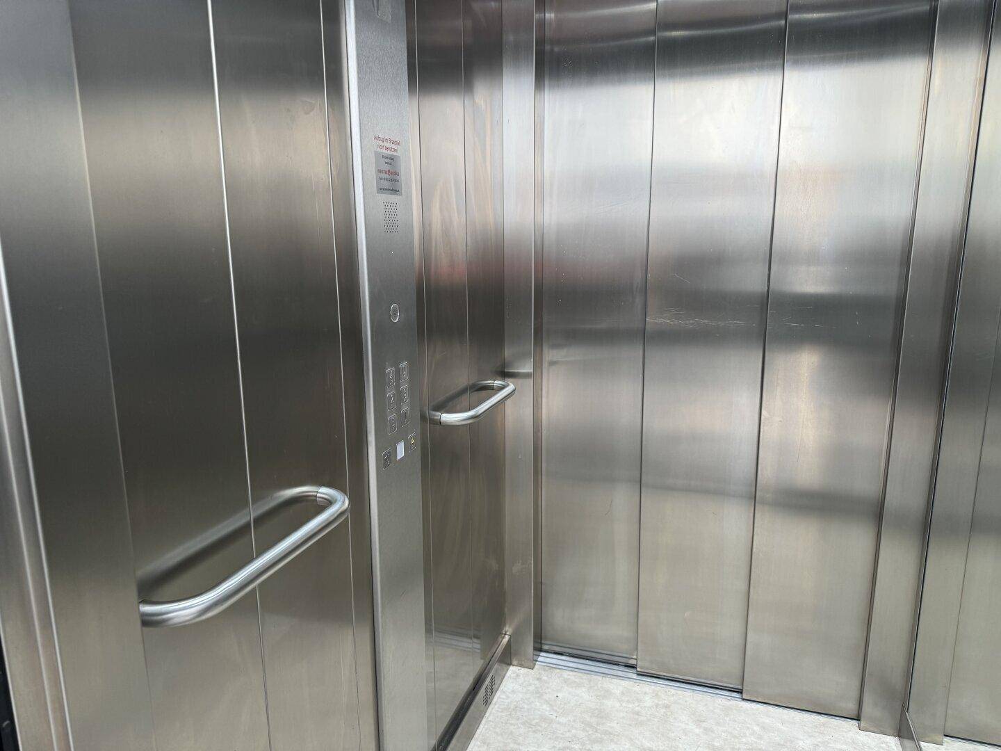 Moderner Aufzug mit Edelstahlverkleidung und Haltegriffen, bietet barrierefreien Zugang zu den Etagen.