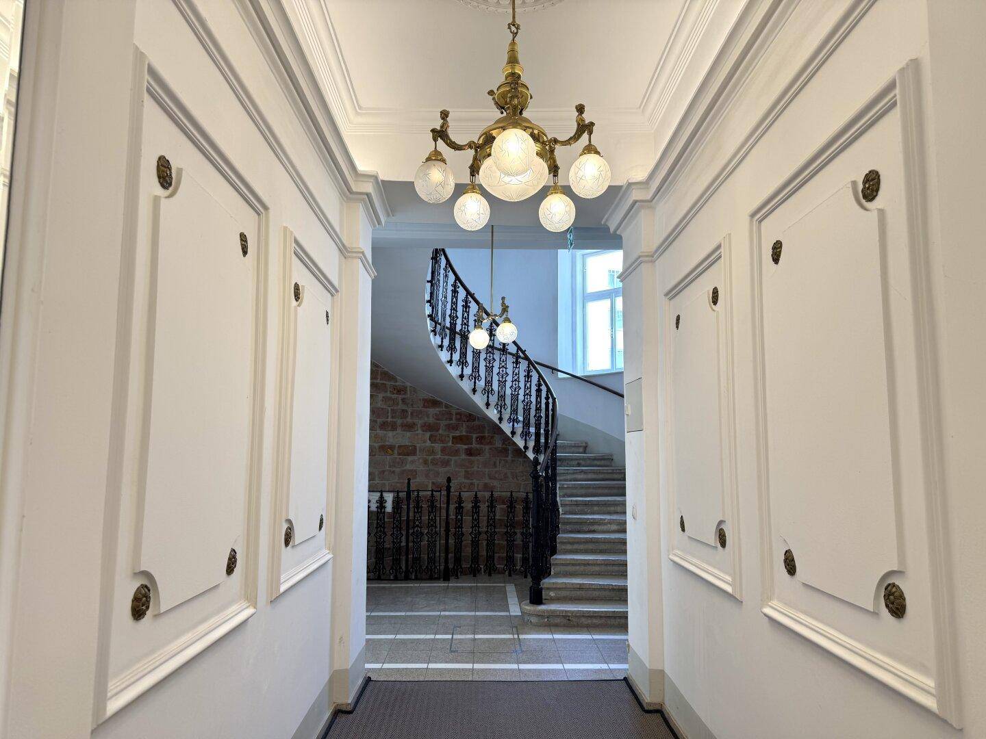 Eleganter Flur mit Stuckdecke und einem prächtigen Kronleuchter, der zu einer geschwungenen Treppe führt.