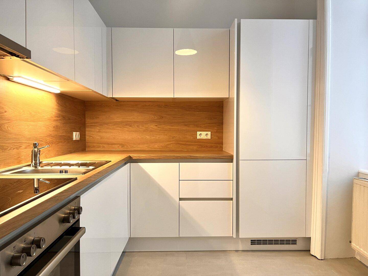 Moderne Küche mit weißen Hochglanzfronten, Holzakzenten und integrierten Elektrogeräten.
