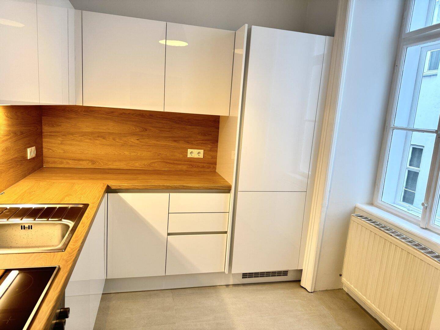 Helle Einbauküche mit weißen Schränken, Holzdetails und Fenster für natürliches Licht.