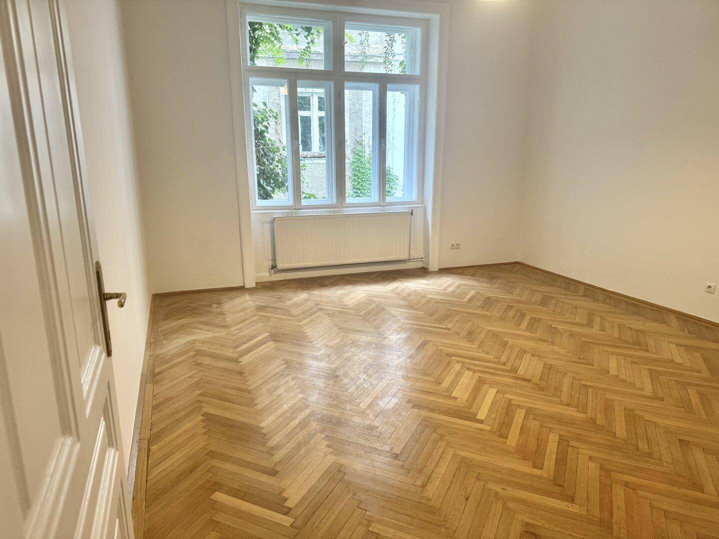 Helles Zimmer mit klassischem Fischgrätparkett und großem Fenster, bereit zur individuellen Gestaltung.