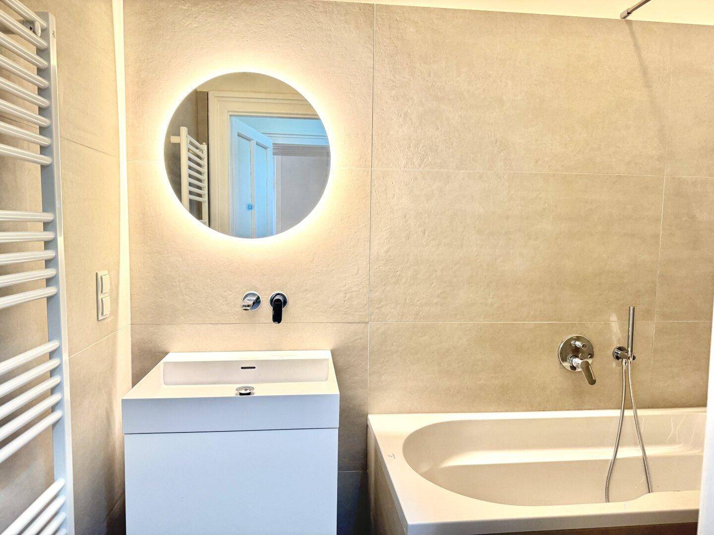 Elegantes Badezimmer mit Badewanne, modernem Waschtisch und beheiztem Handtuchhalter.