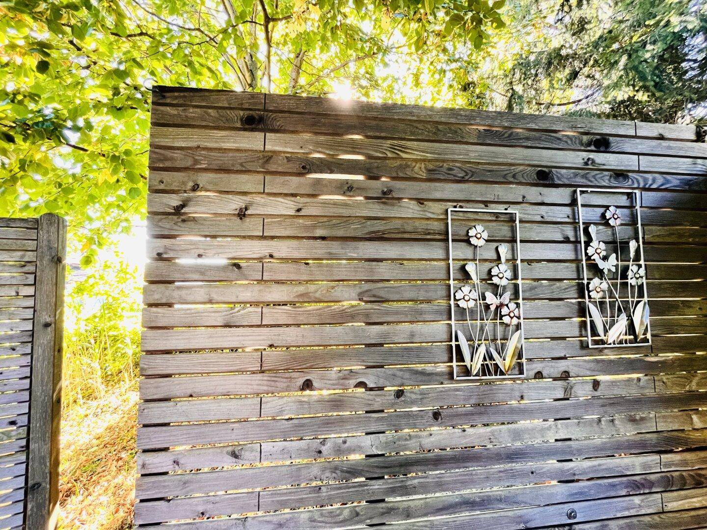 Holzzaun mit dekorativen Metallornamenten im sonnigen Gartenbereich.