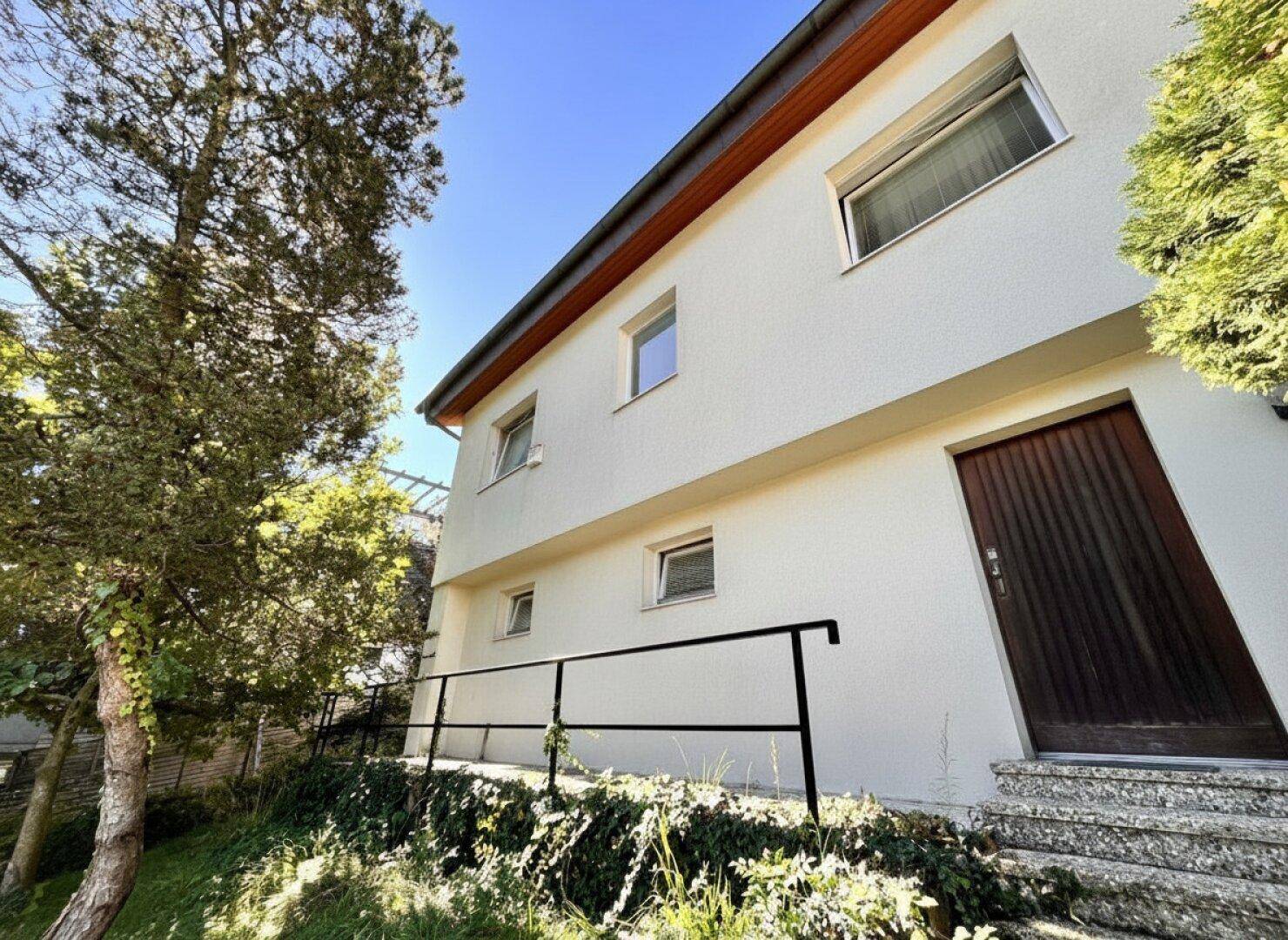 Fassade eines Wohnhauses mit weißem Putz, Holzdetails und Treppenzugang.