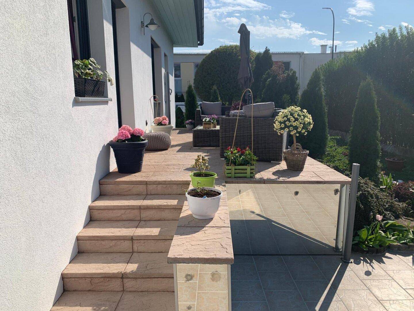 Treppe führt zu einer einladenden Terrasse mit Sitzgelegenheiten und dekorativen Pflanzen.