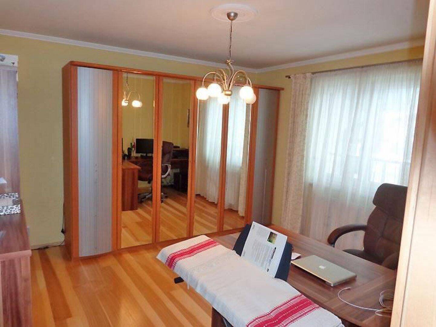 Helles Arbeitszimmer mit Holzfußboden, großem Spiegelschrank und Schreibtisch.