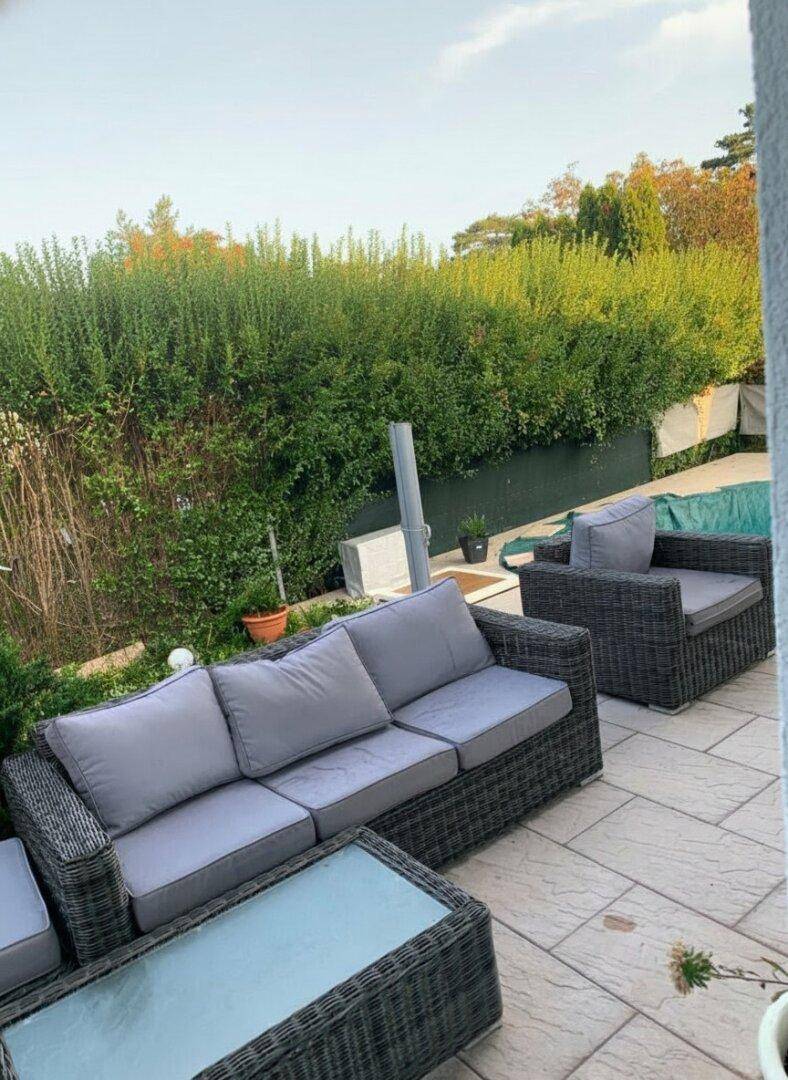 Entspannungsbereich auf der Terrasse mit bequemen Sitzmöbeln und einer hohen Hecke im Hintergrund.