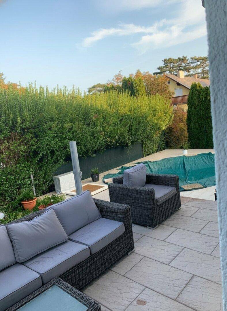Gemütlicher Sitzbereich auf der Terrasse mit Rattanmöbeln und einer dichten Hecke als Sichtschutz.