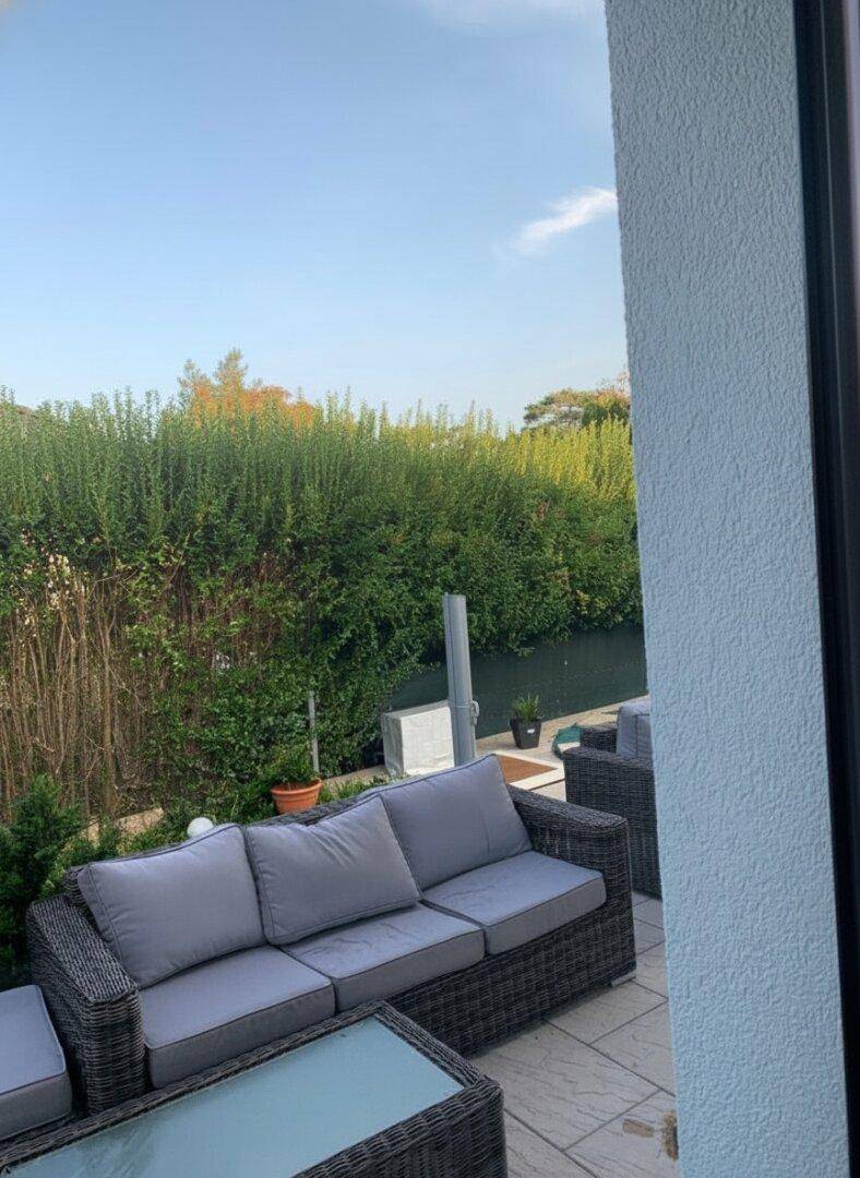 Entspannungsbereich auf der Terrasse mit bequemen Rattanmöbeln und einer hohen, grünen Hecke.