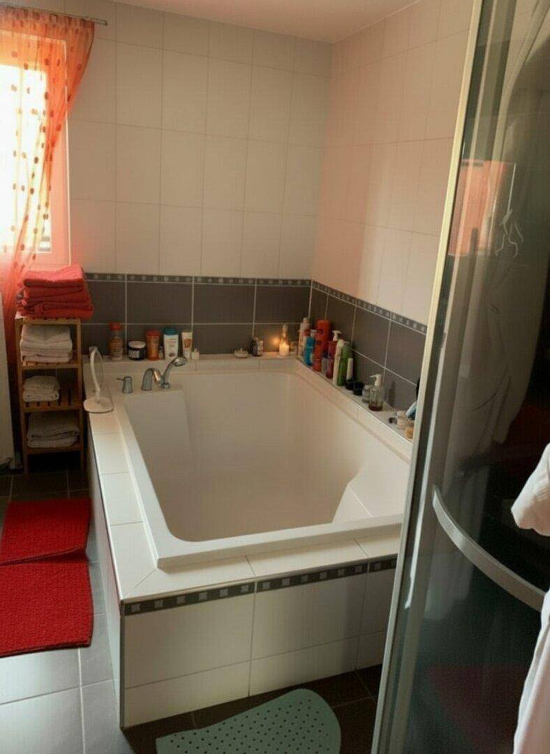 Badezimmer mit einer großen, gefliesten Badewanne und roten Akzenten in der Dekoration.