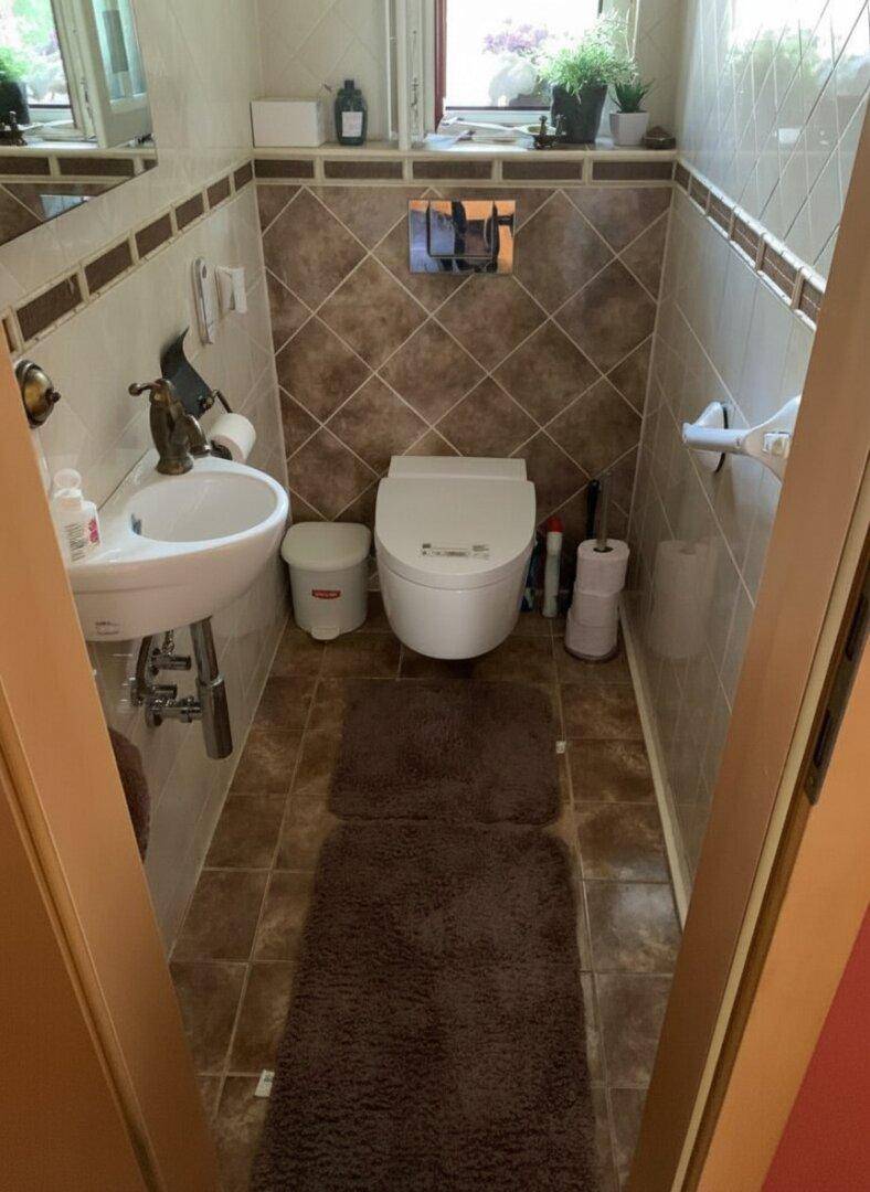 Kleines WC mit Wand-WC, Waschbecken und gemusterten Fliesen an Wänden und Boden.